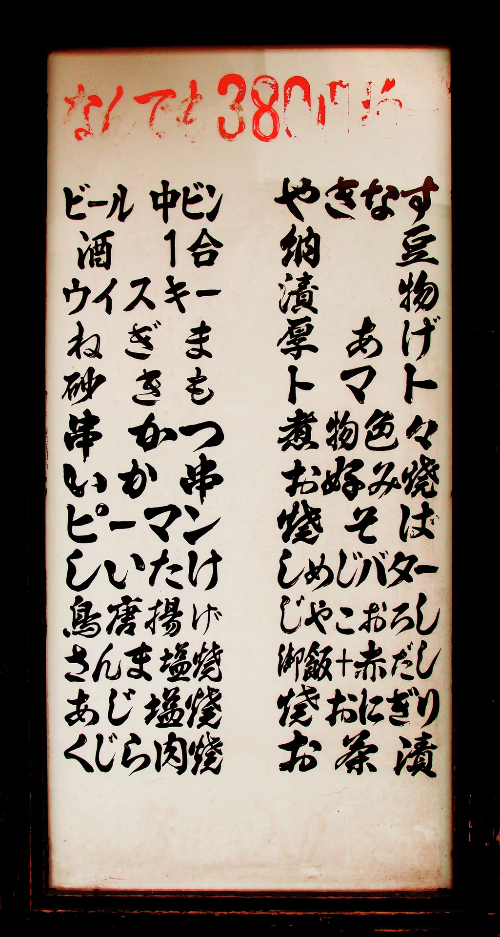 Columns of handwritten black Japanese menu items cover a pale vertical board beneath red price lettering.