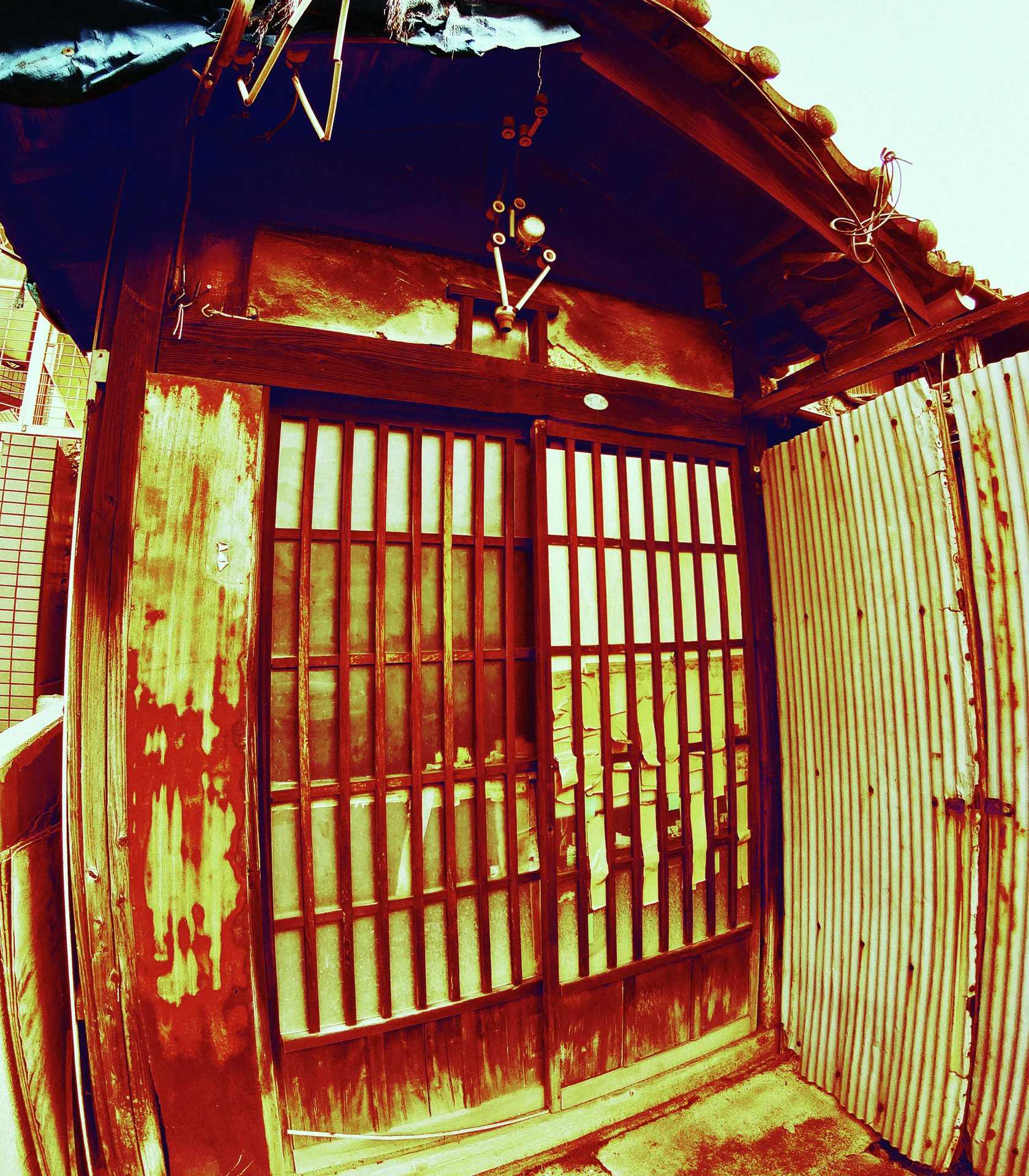 Weathered wooden lattice doors sit beneath a small tiled overhang beside rust-streaked corrugated siding.