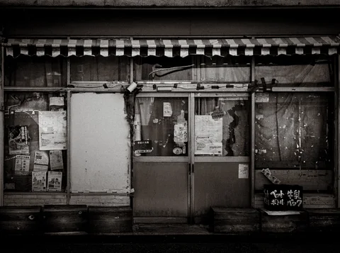Tattered notices cover an aging storefront beneath a striped awning in black and white.