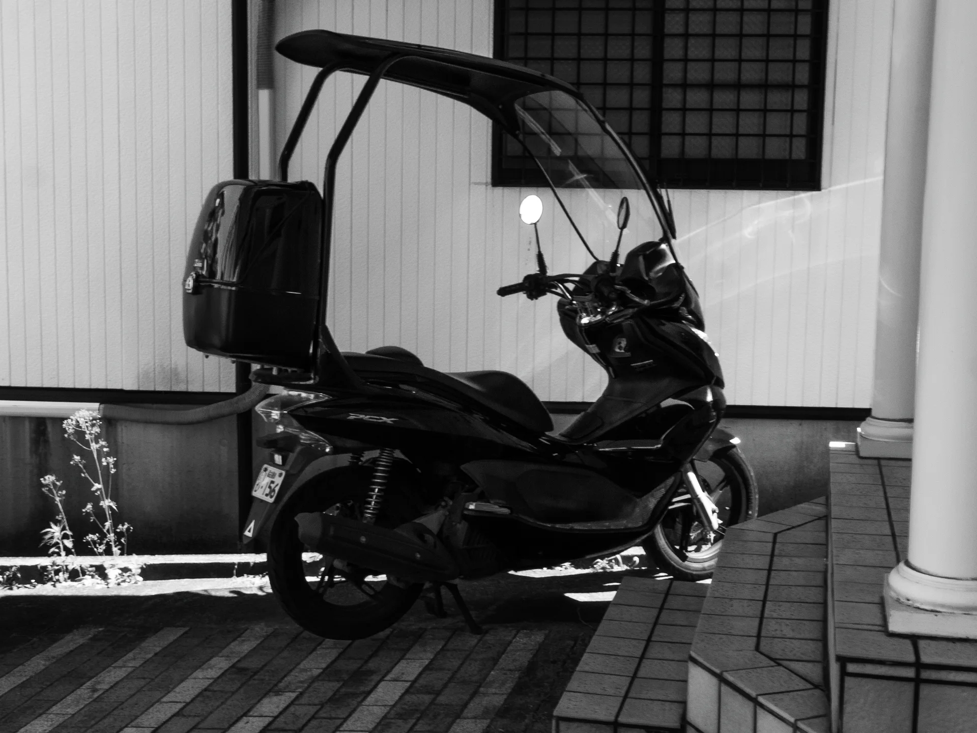 A black scooter with a tall rain canopy stands on brick paving beside tiled entrance steps.