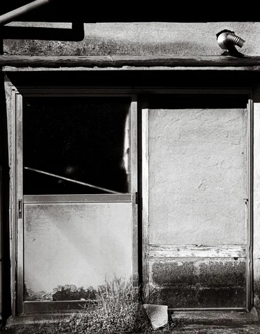 A battered sliding metal doorway has one dark open panel beneath a projecting lamp in black and white.