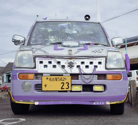 Purple trim, decorative chains, and numerous small ornaments cover the front of a silver compact vehicle.