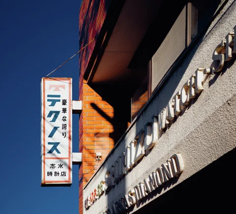 Raised metallic lettering and a projecting vertical sign catch sunlight against a blue sky.